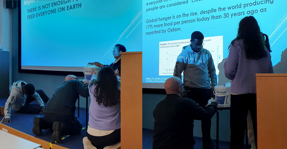 Photo of members of the group presenting a dramatisation of Myth 1, there is not enough food for everyone on Earth and the reality. First scene: One member holding food while others are begging on their knees. Second scene: Members standing surrounding food table.